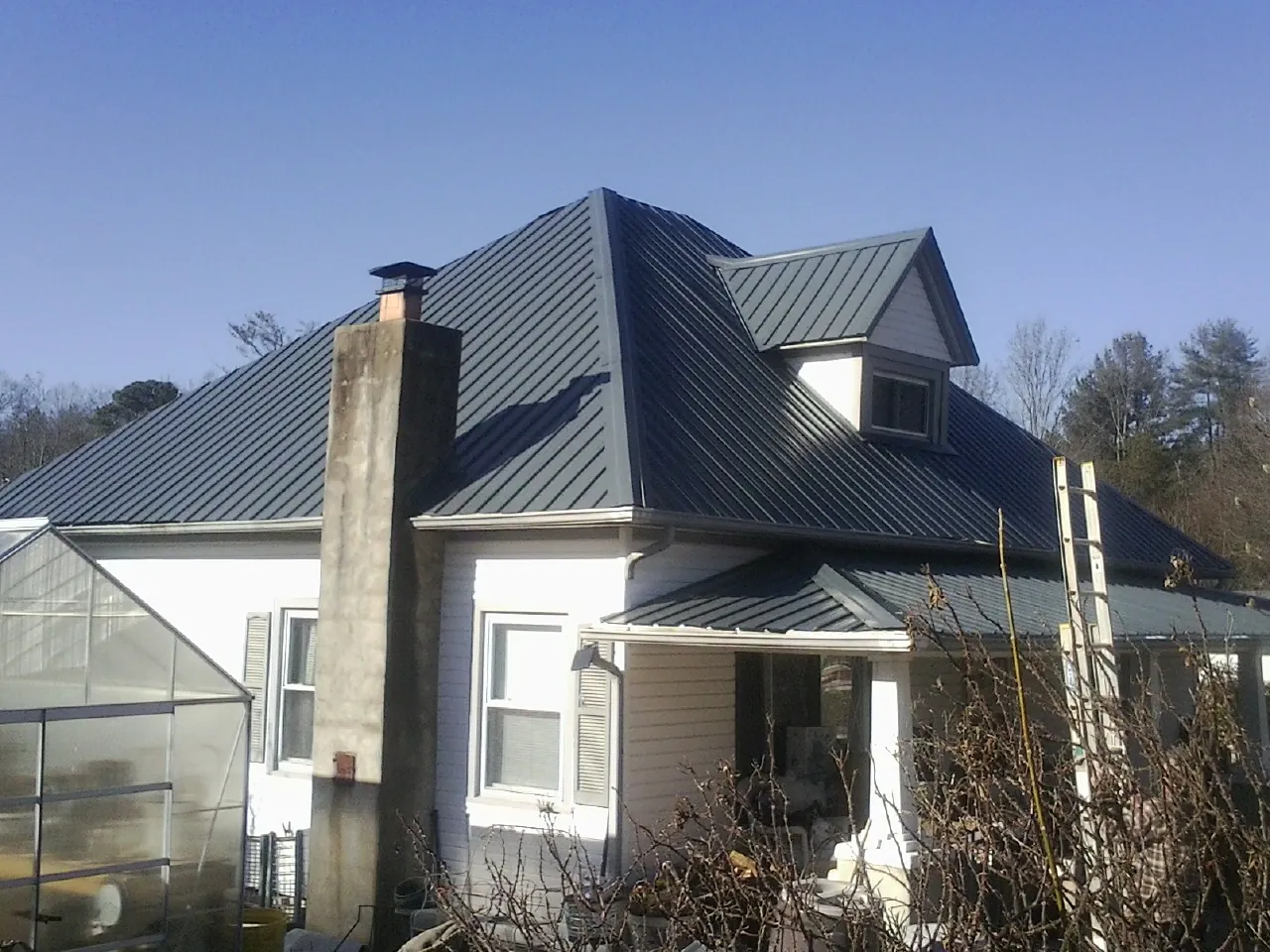 Dark blue standing seam metal roof on a white farmhouse with dormer — Slate & Tile Roof Repair by Roofing Brothers in Amawalk