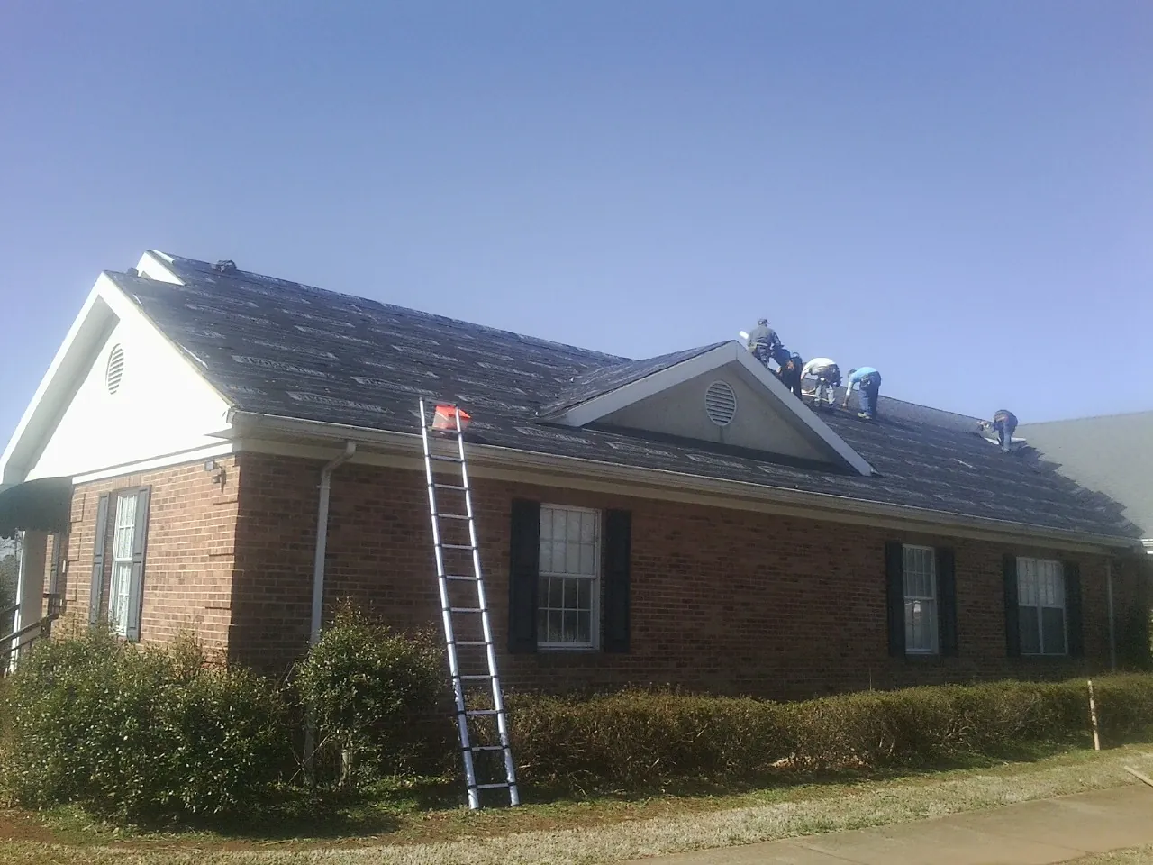 Crew tearing shingles off a brick ranch roof with a ladder set — Emergency Roof Repair work by our crew in Amawalk