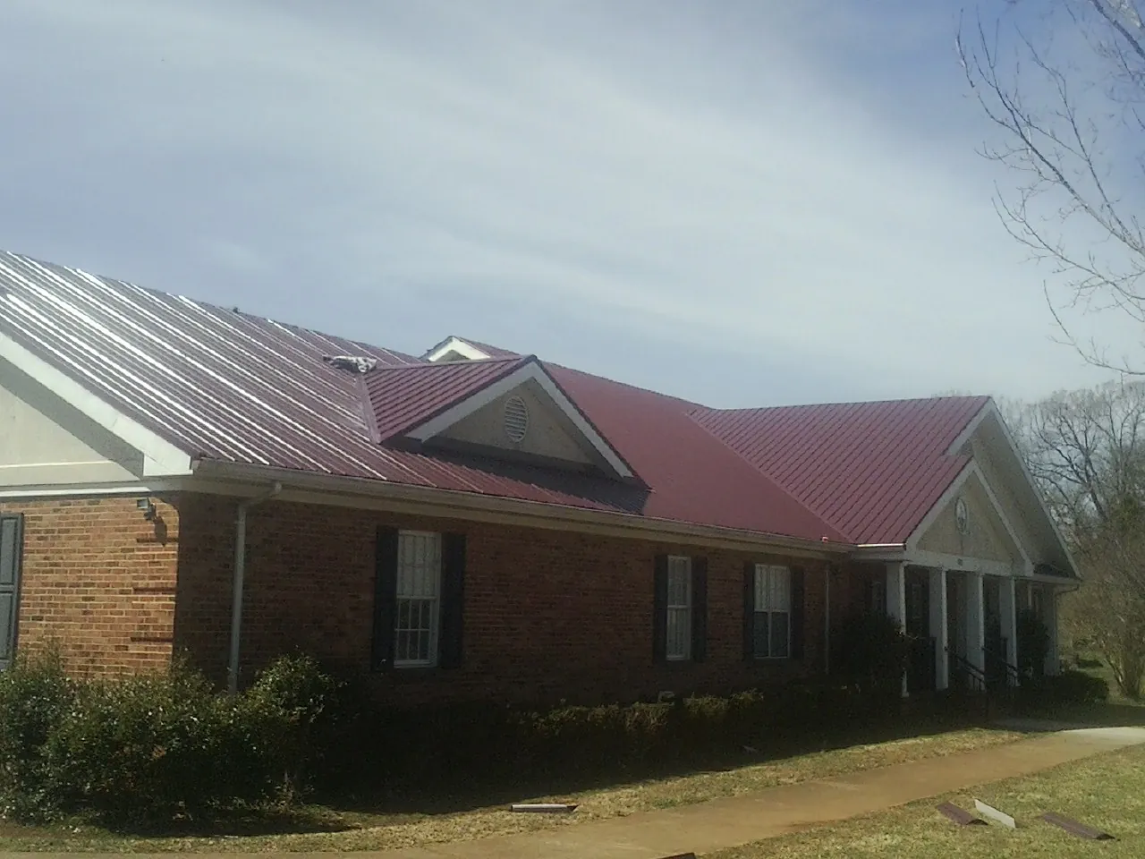 Red metal roof with gabled entries on a long brick building, from a Hail Damage Roof Repair job in Amawalk