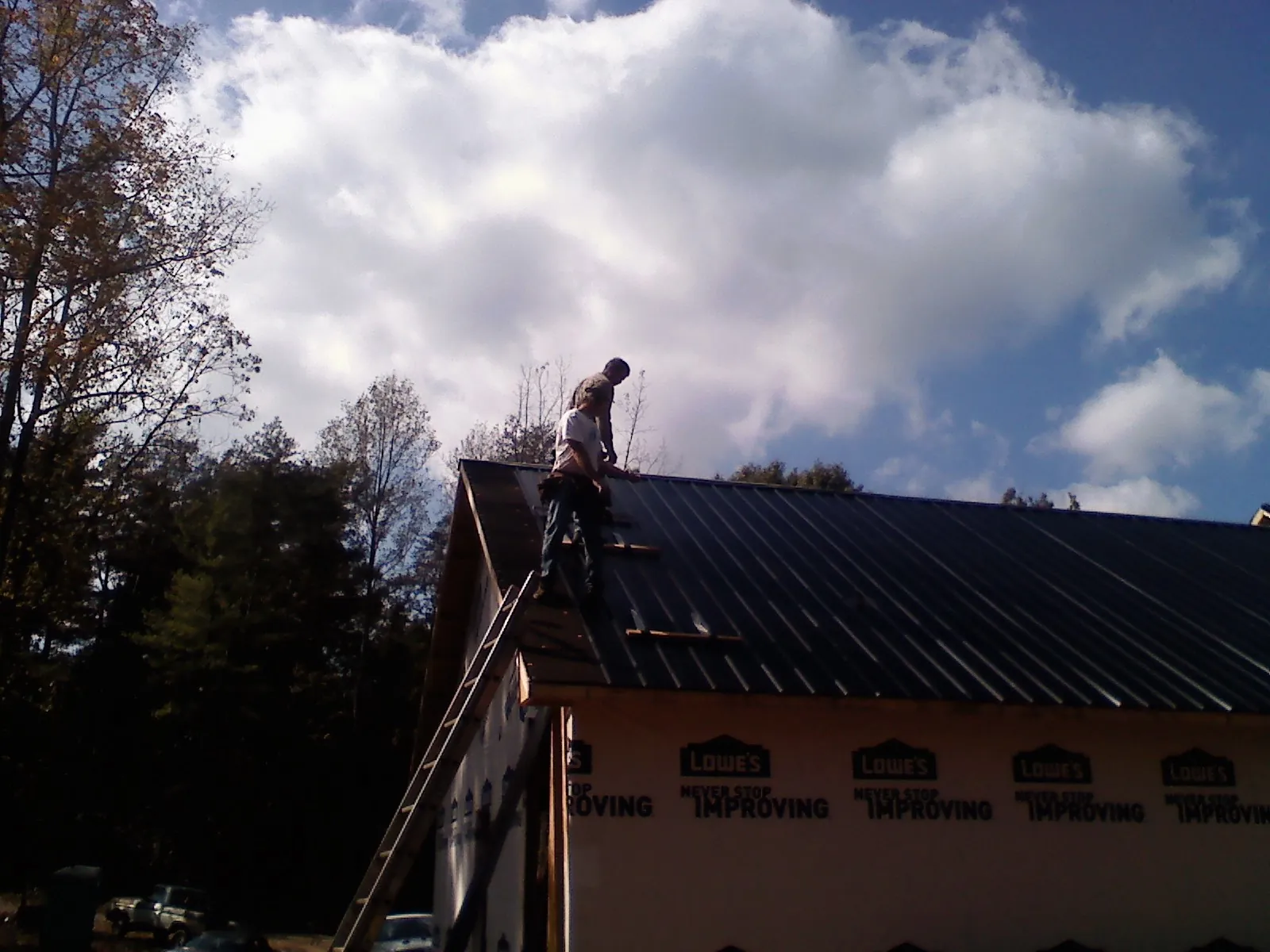 Roofer fastening dark metal panels high against a cloudy sky, from a Roof Inspection job in Amawalk