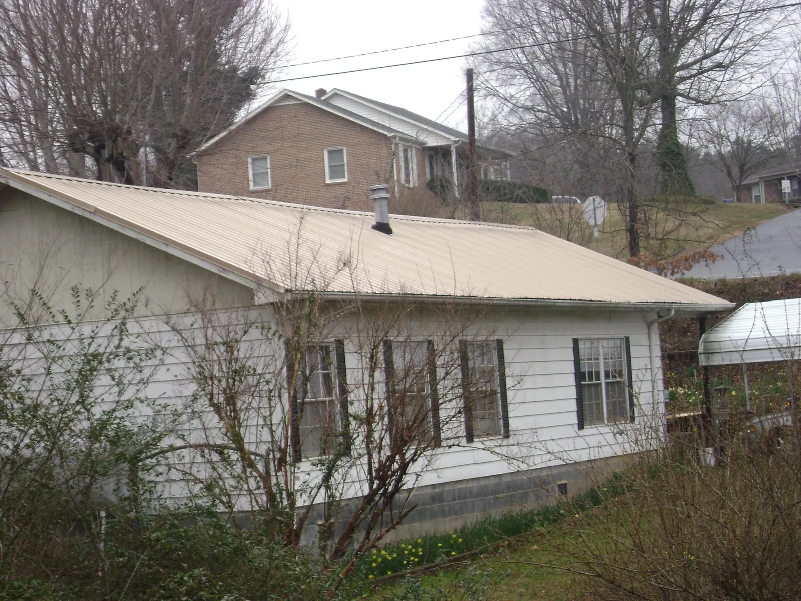 Tan metal roof on a white sided house set into a hillside — Commercial Roofing by Roofing Brothers in Amawalk